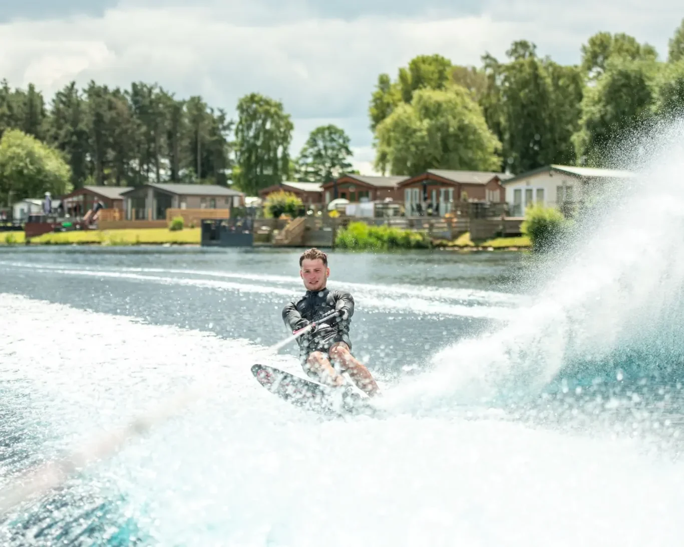 A person water skiing on a lake with trees and cabins in the background.